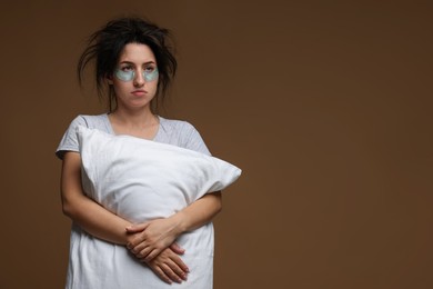 Photo of Woman with eye patches and pillow suffering from hangover on brown background, space for text
