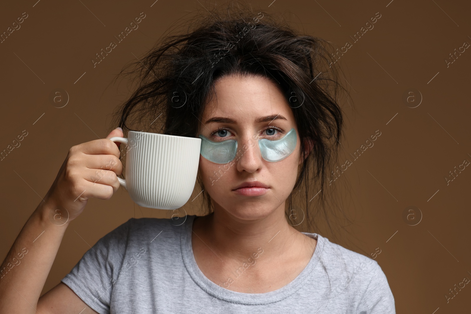 Woman with eye patches and cup of drink suffering from hangover on brown background Photo of Woman with eye patches and cup of drink suffering from hangover on brown background