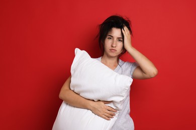 Photo of Woman with pillow suffering from hangover on red background