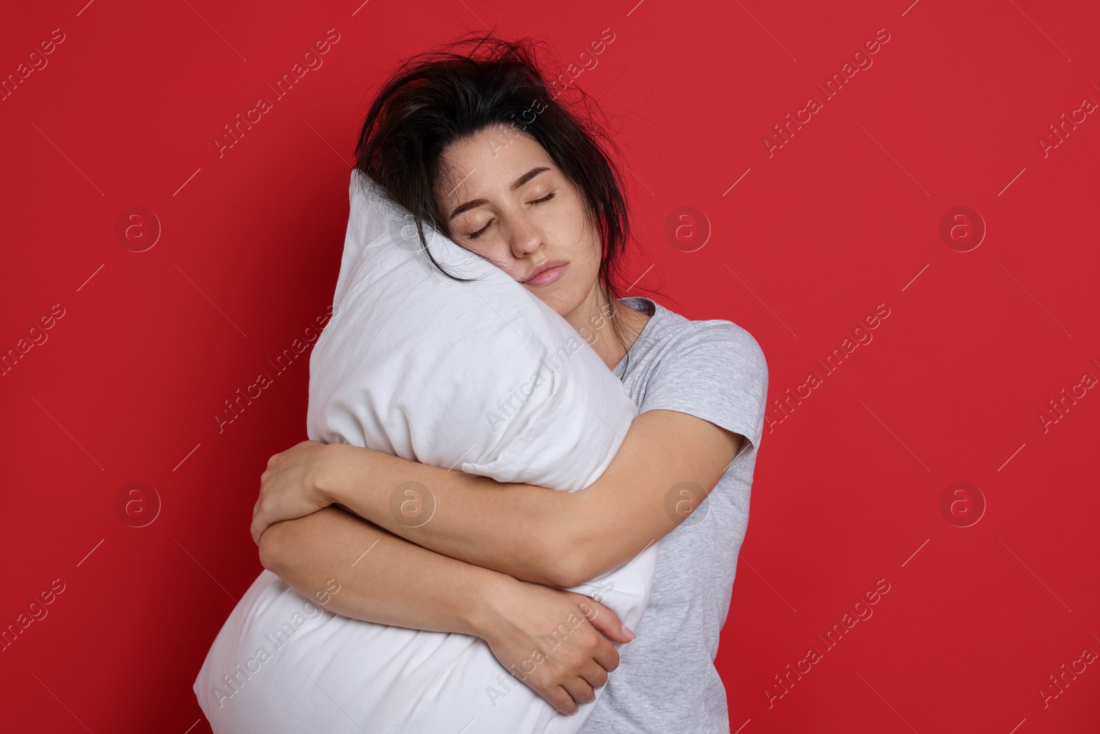 Woman with pillow suffering from hangover on red background Photo of Woman with pillow suffering from hangover on red background