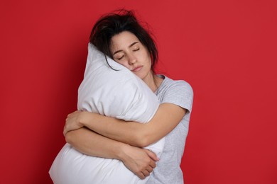 Photo of Woman with pillow suffering from hangover on red background