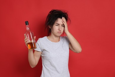 Photo of Woman with bottle of whiskey suffering from hangover on red background