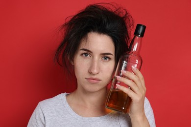 Photo of Woman with bottle of whiskey suffering from hangover on red background