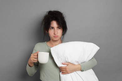 Photo of Woman with pillow and cup of drink suffering from hangover on grey background