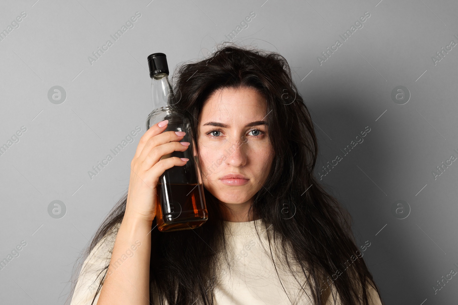 Woman with bottle of whiskey suffering from hangover on grey background Photo of Woman with bottle of whiskey suffering from hangover on grey background