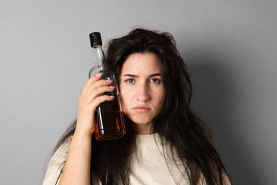 Photo of Woman with bottle of whiskey suffering from hangover on grey background