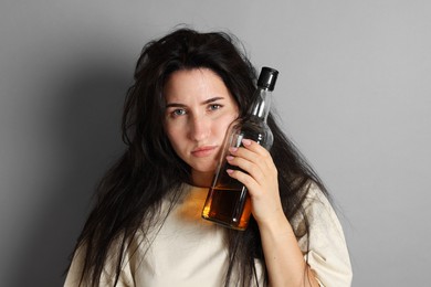 Photo of Woman with bottle of whiskey suffering from hangover on grey background