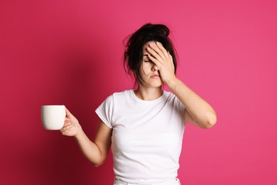 Photo of Woman with cup of drink suffering from hangover on crimson background