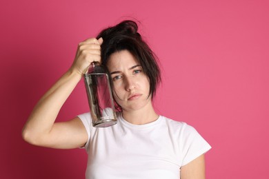Photo of Woman with bottle of alcohol drink suffering from hangover on crimson background