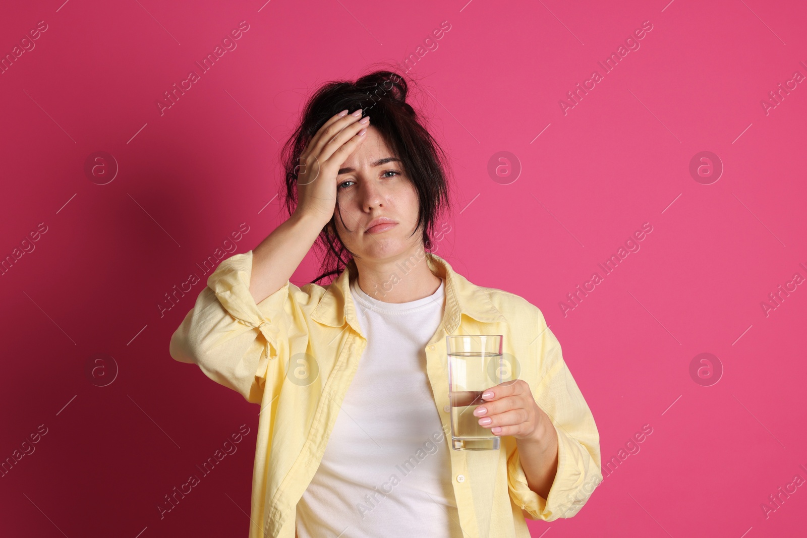 Woman with glass of water suffering from hangover on crimson background Photo of Woman with glass of water suffering from hangover on crimson background