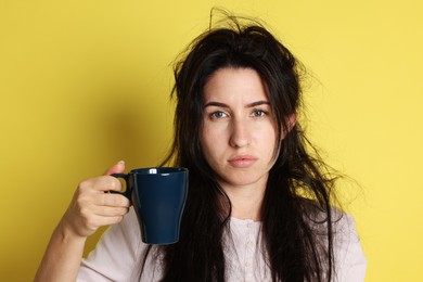 Photo of Woman with cup of drink suffering from hangover on yellow background