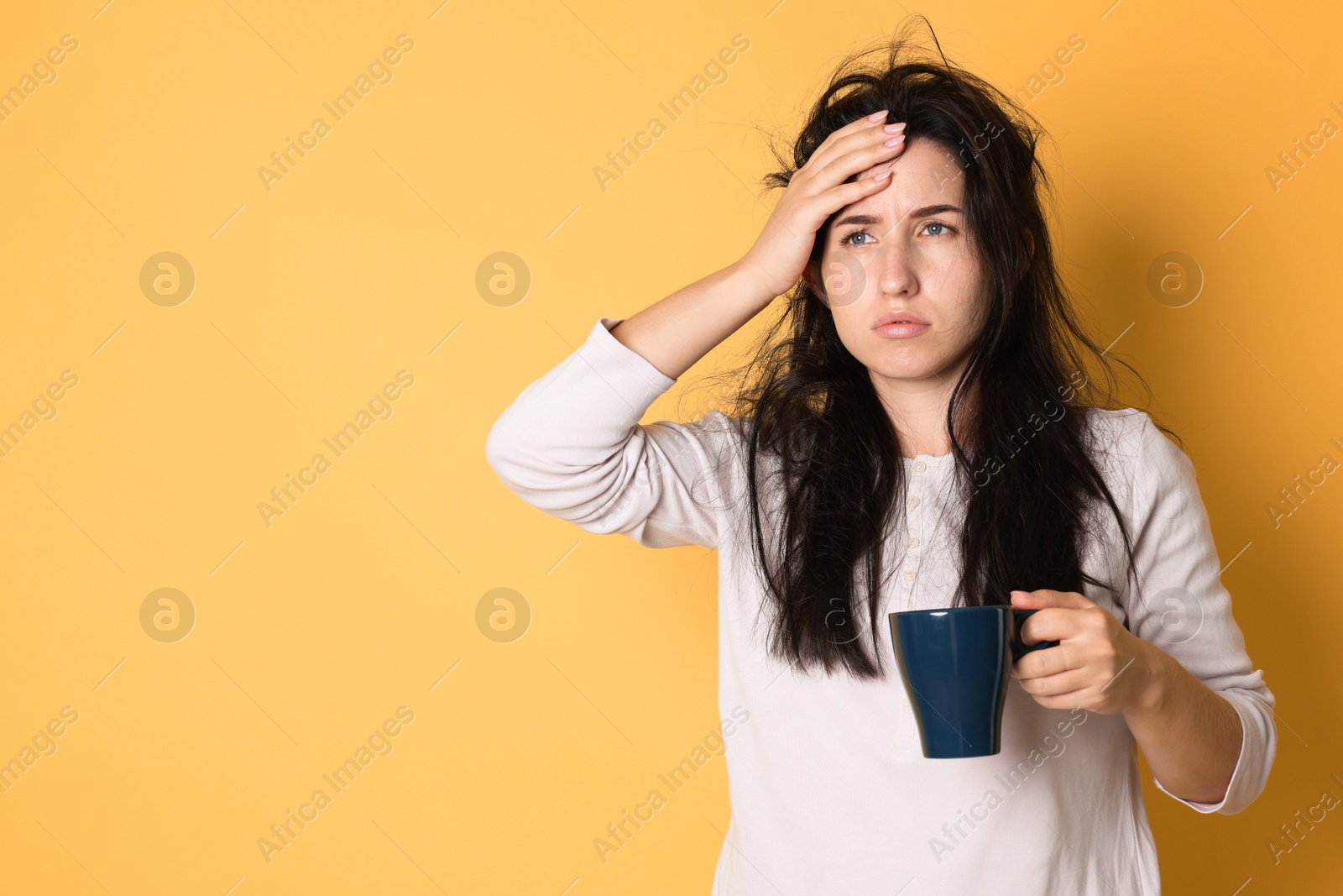 Woman with cup of drink suffering from hangover on orange background, space for text Photo of Woman with cup of drink suffering from hangover on orange background, space for text