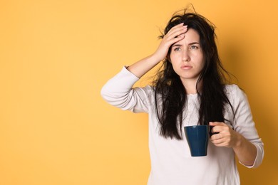 Photo of Woman with cup of drink suffering from hangover on orange background, space for text