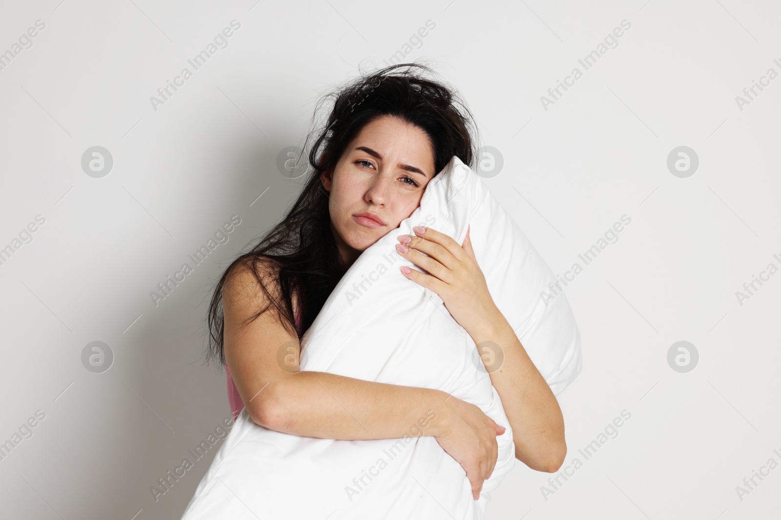 Photo of Woman with pillow suffering from hangover on light grey background