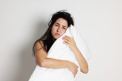 Photo of Woman with pillow suffering from hangover on light grey background