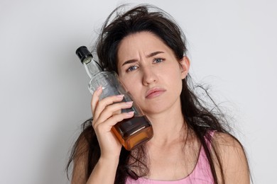 Photo of Woman with bottle of whiskey suffering from hangover on light grey background