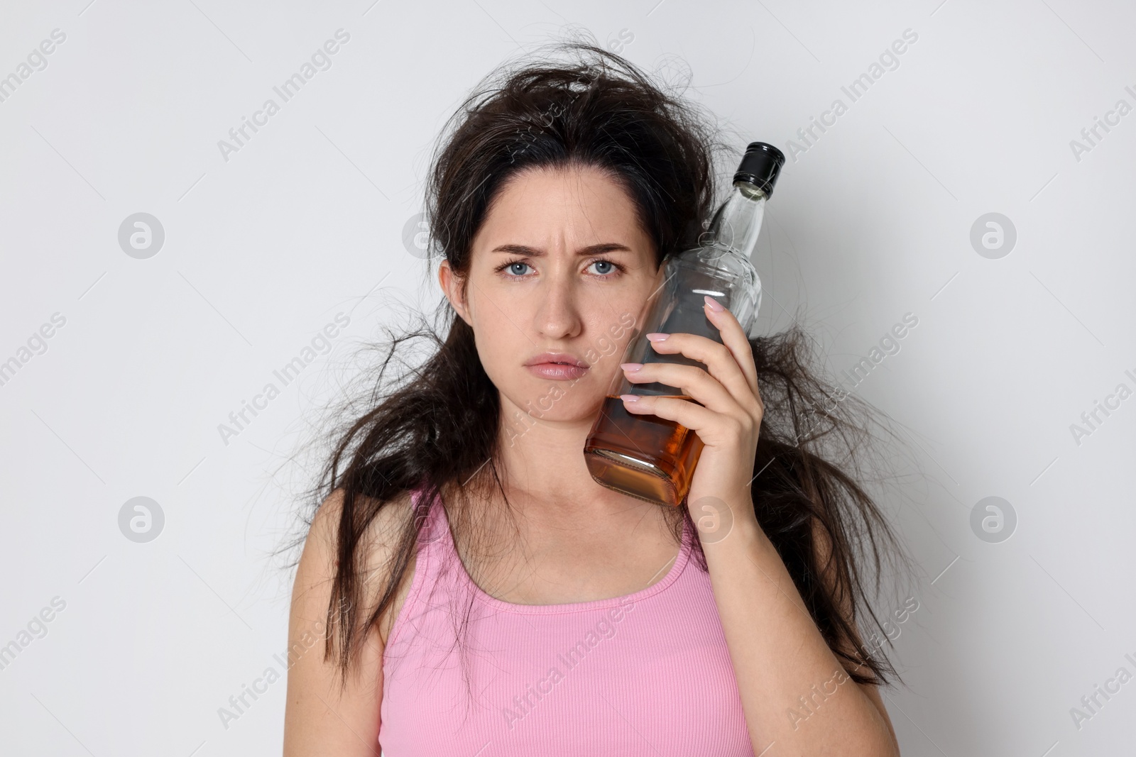 Woman with bottle of whiskey suffering from hangover on light grey background Photo of Woman with bottle of whiskey suffering from hangover on light grey background