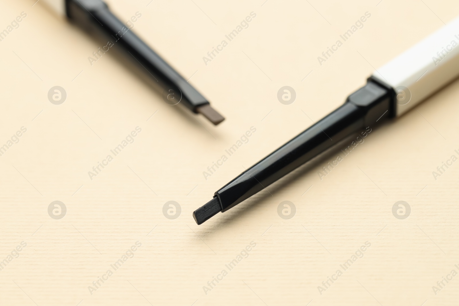 Photo of Automatic eyebrow pencils on beige background, macro view