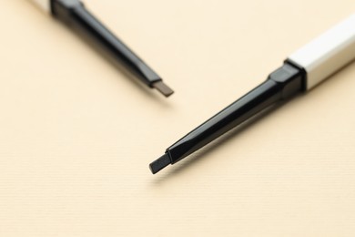 Photo of Automatic eyebrow pencils on beige background, macro view