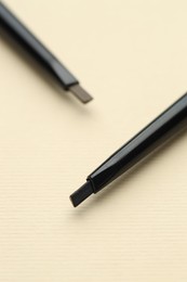 Photo of Automatic eyebrow pencils on beige background, macro view