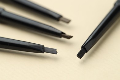Photo of Automatic eyebrow pencils on beige background, macro view