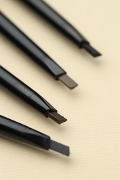 Photo of Automatic eyebrow pencils on beige background, macro view