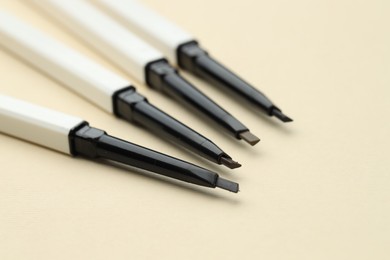 Photo of Automatic eyebrow pencils on beige background, closeup