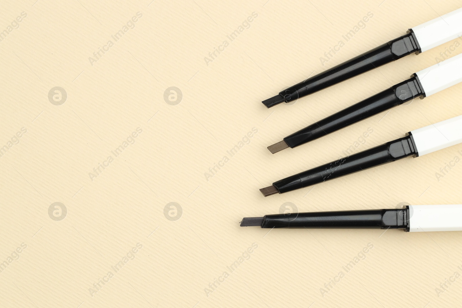 Automatic eyebrow pencils on beige background, flat lay. Space for text Photo of Automatic eyebrow pencils on beige background, flat lay. Space for text