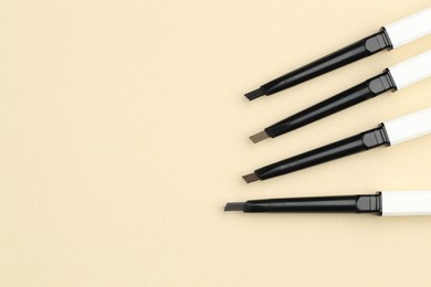 Photo of Automatic eyebrow pencils on beige background, flat lay. Space for text