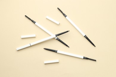 Photo of Automatic eyebrow pencils on beige background, flat lay