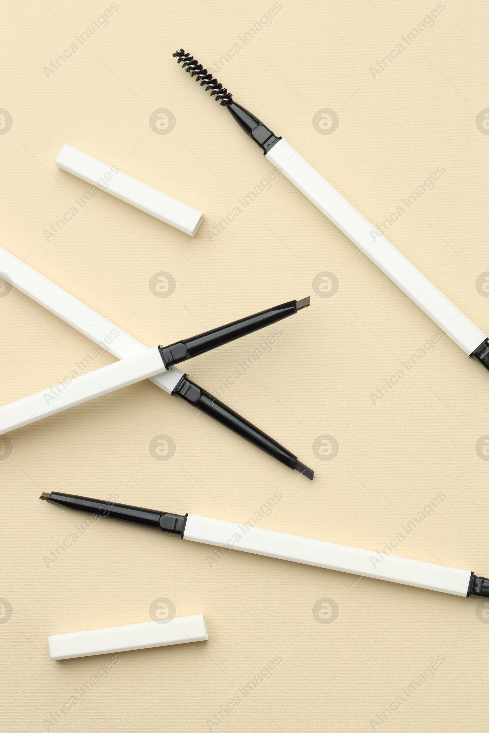 Automatic eyebrow pencils on beige background, flat lay Photo of Automatic eyebrow pencils on beige background, flat lay