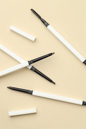 Photo of Automatic eyebrow pencils on beige background, flat lay