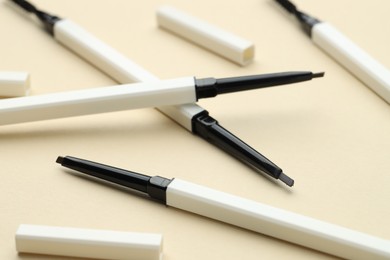 Photo of Automatic eyebrow pencils on beige background, closeup