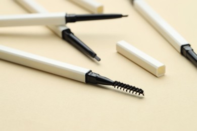 Photo of Automatic eyebrow pencils on beige background, closeup