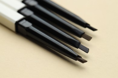 Photo of Automatic eyebrow pencils on beige background, macro view