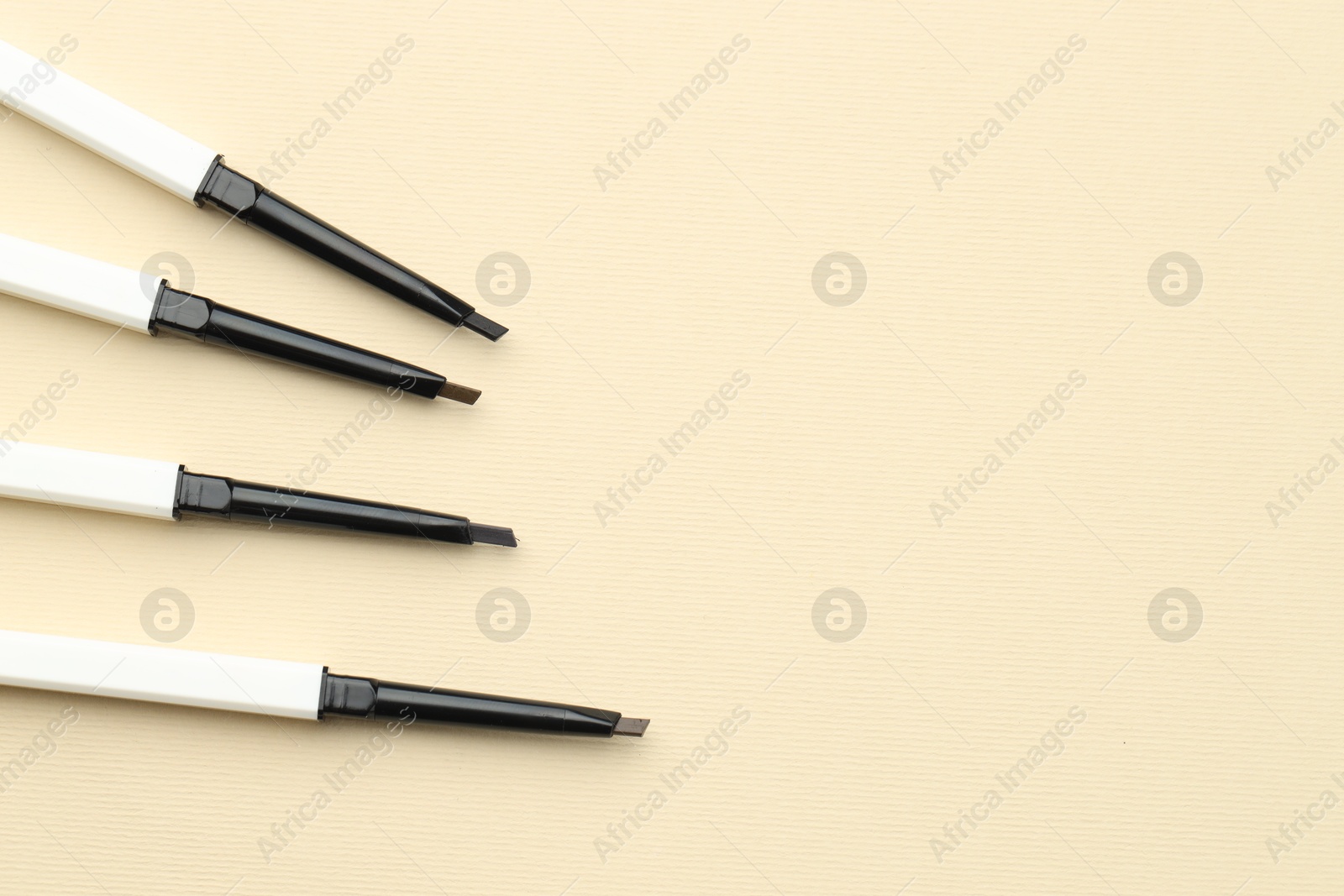 Automatic eyebrow pencils on beige background, flat lay. Space for text Photo of Automatic eyebrow pencils on beige background, flat lay. Space for text