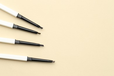 Photo of Automatic eyebrow pencils on beige background, flat lay. Space for text