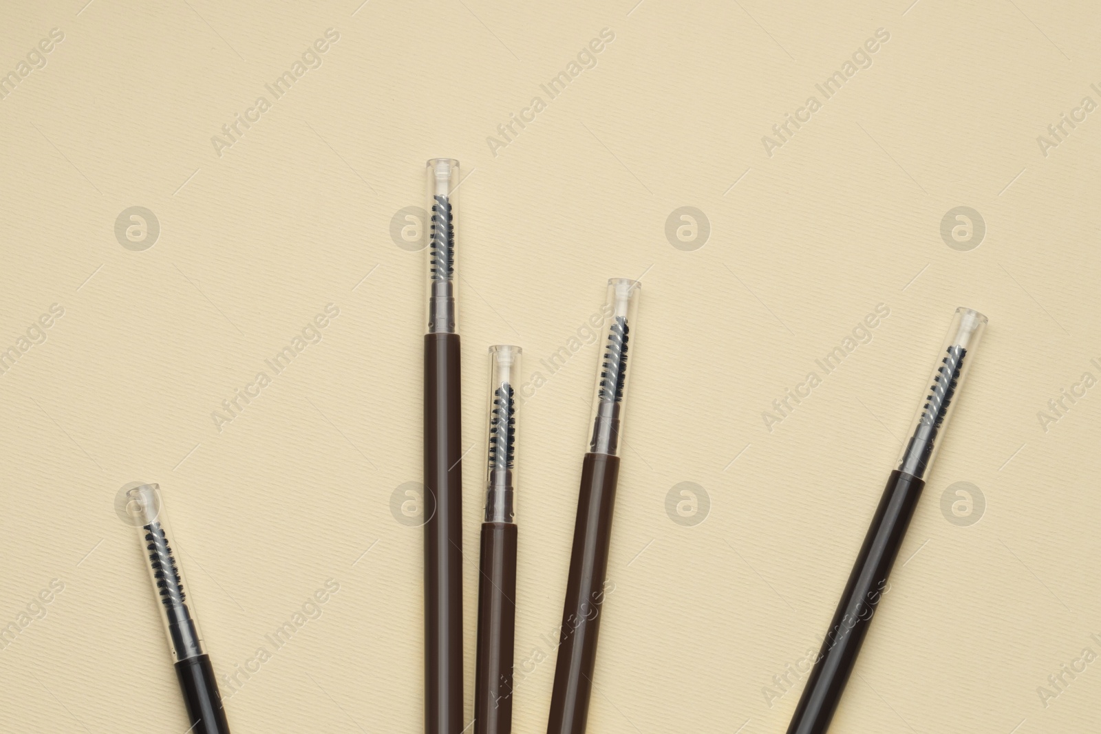 Automatic eyebrow pencils on beige background, flat lay Photo of Automatic eyebrow pencils on beige background, flat lay