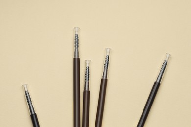 Photo of Automatic eyebrow pencils on beige background, flat lay
