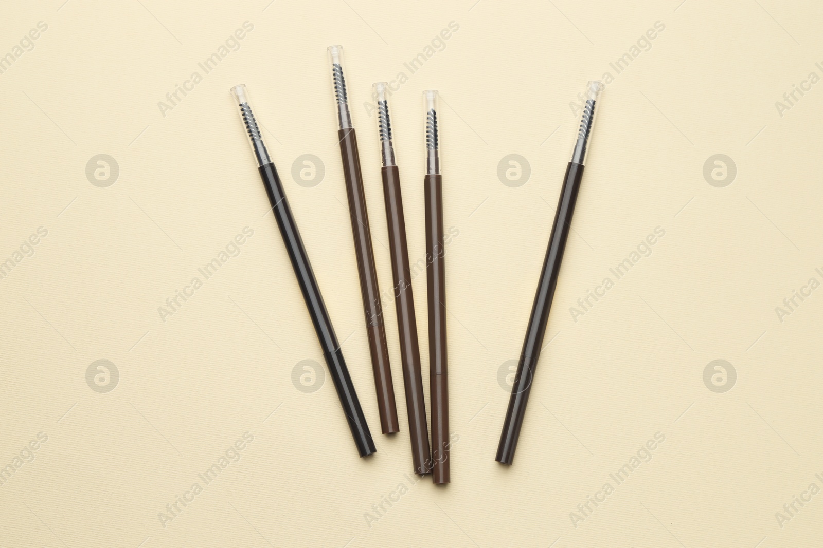 Automatic eyebrow pencils on beige background, flat lay Photo of Automatic eyebrow pencils on beige background, flat lay