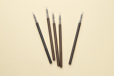 Photo of Automatic eyebrow pencils on beige background, flat lay