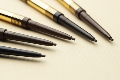 Photo of Automatic eyebrow pencils on beige background, closeup