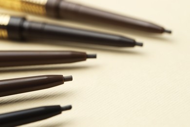 Photo of Automatic eyebrow pencils on beige background, closeup