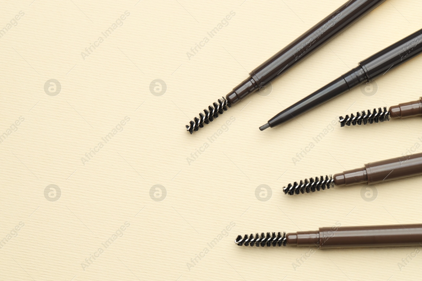 Automatic eyebrow pencils on beige background, flat lay. Space for text Photo of Automatic eyebrow pencils on beige background, flat lay. Space for text