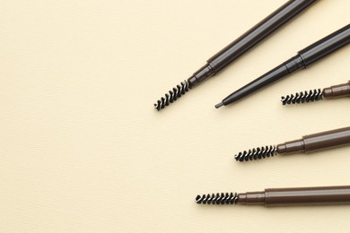 Photo of Automatic eyebrow pencils on beige background, flat lay. Space for text