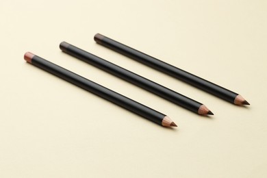 Photo of Different eyebrow pencils on beige background, closeup