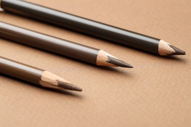 Photo of Different eyebrow pencils on brown background, closeup