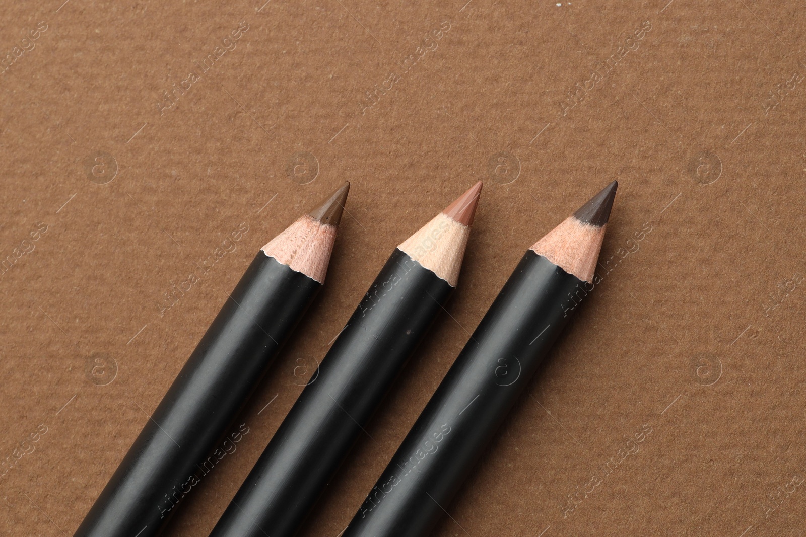 Different eyebrow pencils on brown background, flat lay Photo of Different eyebrow pencils on brown background, flat lay