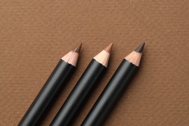 Photo of Different eyebrow pencils on brown background, flat lay