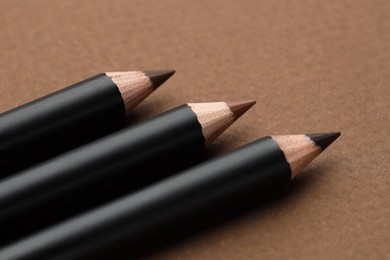Photo of Different eyebrow pencils on brown background, closeup